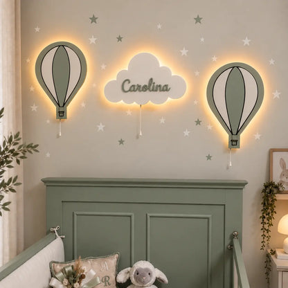 Habitación infantil decorada con set de 3 lámparas de madera: dos globos aerostáticos y nube personalizada con luz LED. Decoración de pared en tonos verdes y blancos.
