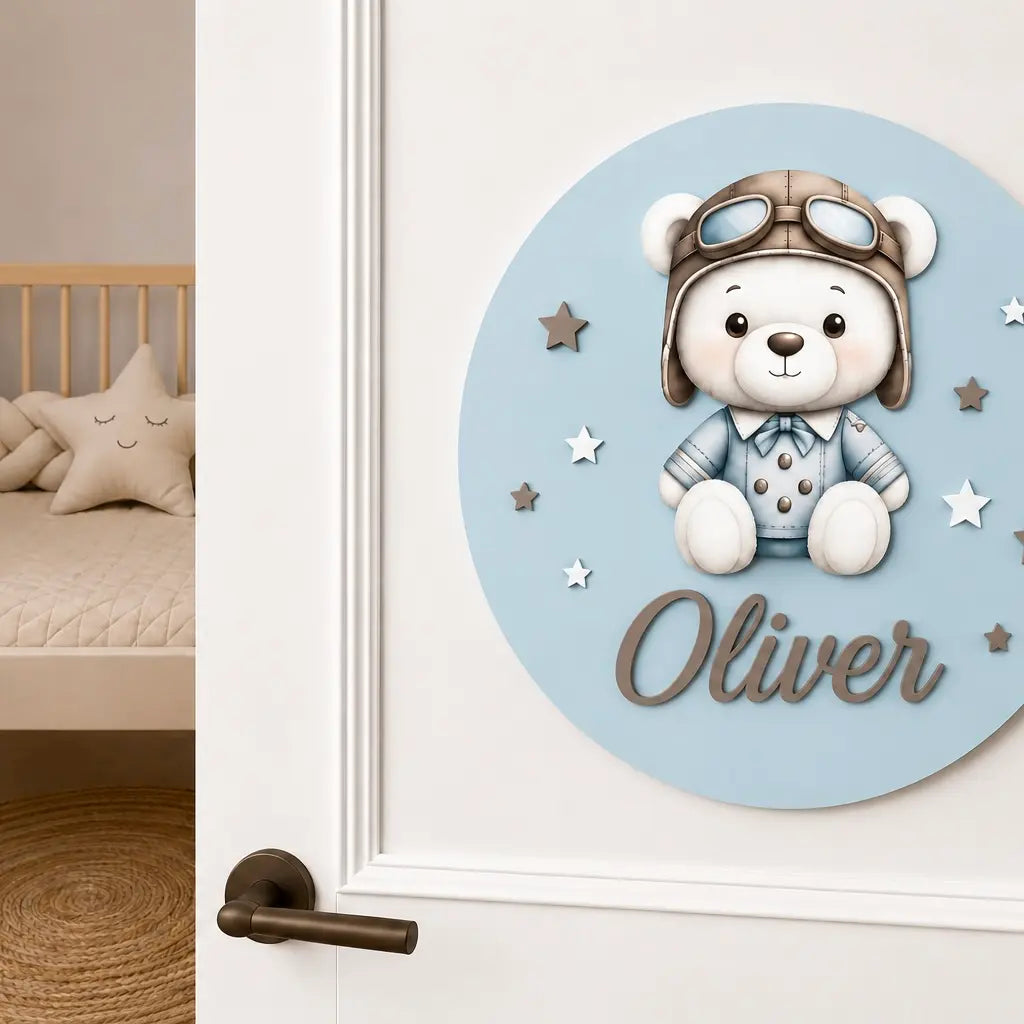 Adorno de madera azul con osito aviador y el nombre Oliver, colgado en la puerta de una habitación infantil.