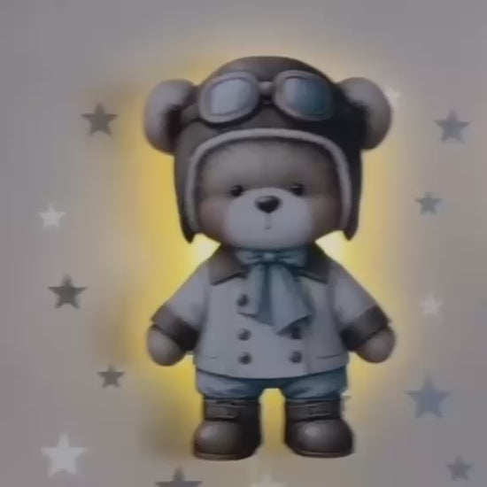 Vídeo de la lámpara del osito aviador con gorro de piloto, encendida con luz cálida sobre una pared con estrellas.